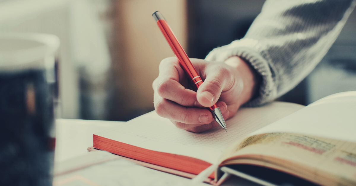 image of a person writing in a journal with an orange pen